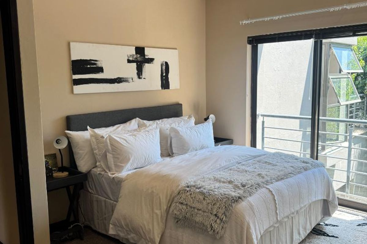 Spacious bedroom featuring high ceilings, a clerestory window for natural light, and sliding glass doors providing access to a private balcony.