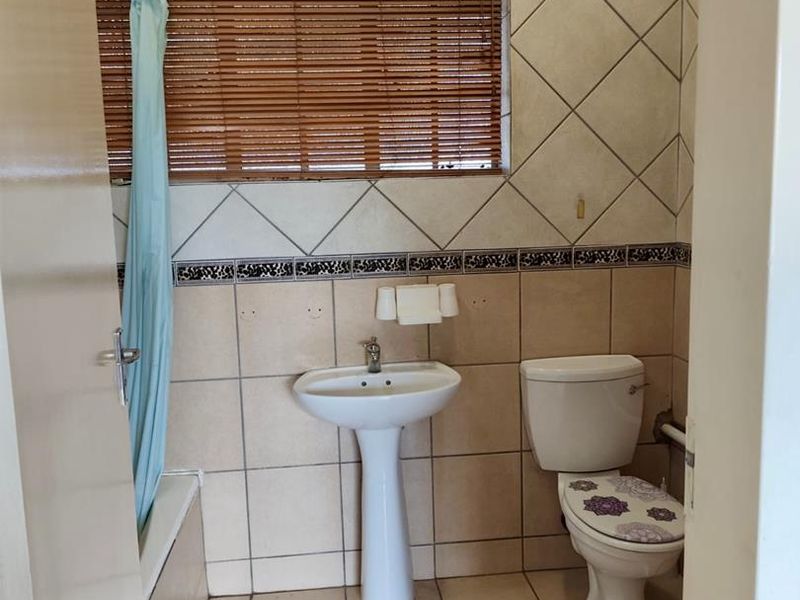 A functional bathroom featuring a pedestal basin, toilet, and bathtub with tiled walls and flooring, offering a classic layout ready for cosmetic updates.