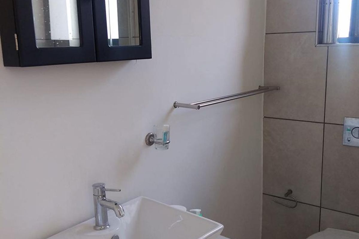 A functional bathroom featuring a wall-mounted vanity basin, a wall-hung toilet, and a mirrored medicine cabinet with neutral wall and floor tiling.