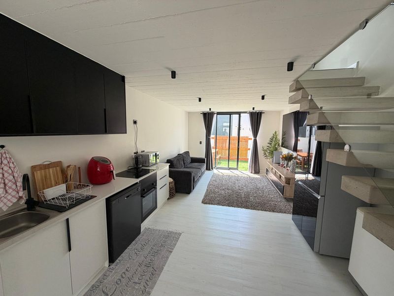 Modern open-plan living area featuring a sleek kitchen with built-in appliances, a concrete staircase, and direct access to a private outdoor space.