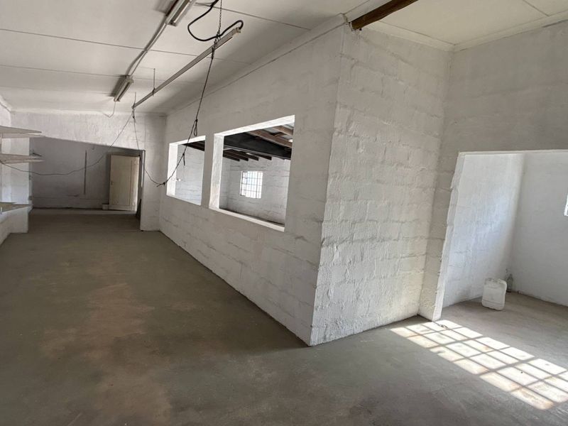An open-plan industrial utility space featuring painted masonry walls, exposed ceiling beams, and security-barred windows, suitable for storage or workshop use.