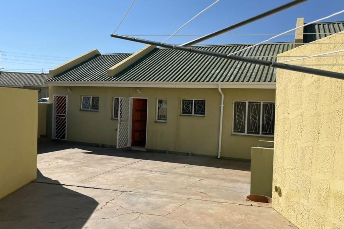 Rear exterior view of the townhouse featuring a paved courtyard, security gates, and metal roofing.