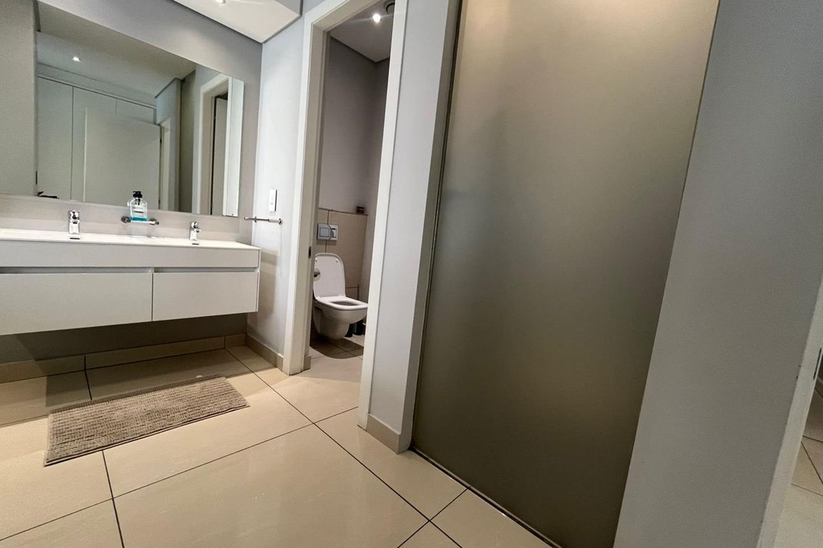 Modern bathroom featuring a wall-mounted double vanity with integrated sinks, large mirror, and a separate enclosed toilet area with tiled flooring.