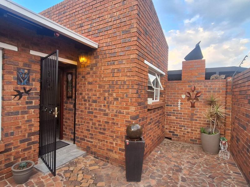 A well-maintained face-brick entrance courtyard featuring paved flooring, a secure entrance gate, and a built-in chimney structure.
