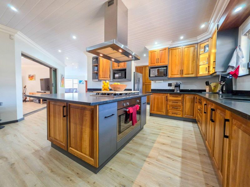 Modern kitchen featuring a central island with built-in oven and cooktop, complemented by wooden cabinetry, stone countertops, and recessed lighting.