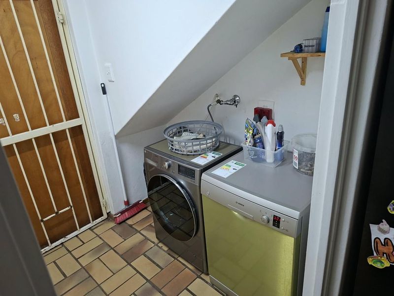 A functional under-stair laundry area featuring tiled flooring, plumbing connections for appliances, and a secure access door.