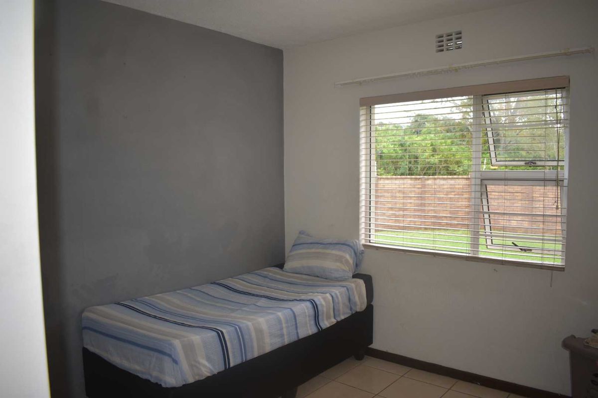 A simple bedroom featuring tiled flooring, a window with fitted blinds, and a grey accent wall.
