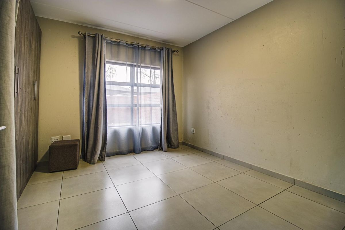 A vacant bedroom featuring neutral tiled flooring and a built-in wardrobe, offering a clean canvas for personalization.