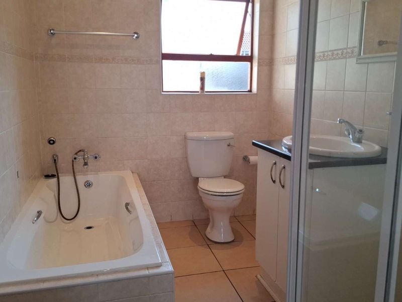 A functional bathroom featuring a built-in bathtub, separate shower enclosure, vanity with basin, and neutral wall and floor tiling.