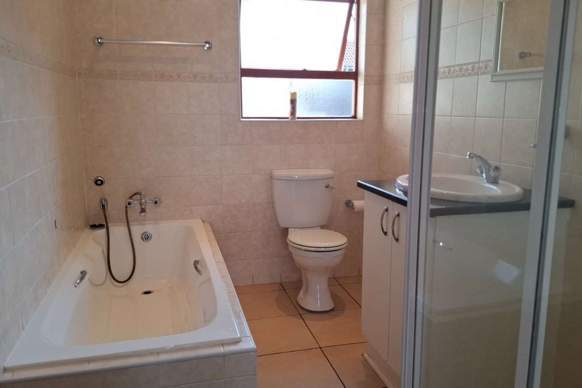A functional bathroom featuring a built-in bathtub, separate shower enclosure, vanity with basin, and neutral wall and floor tiling.