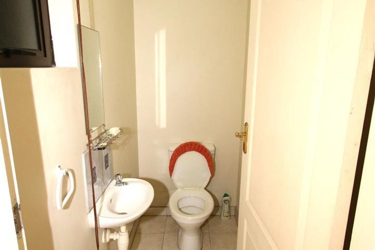 A compact guest cloakroom featuring a wall-mounted basin and a standard toilet, finished with neutral floor tiling.