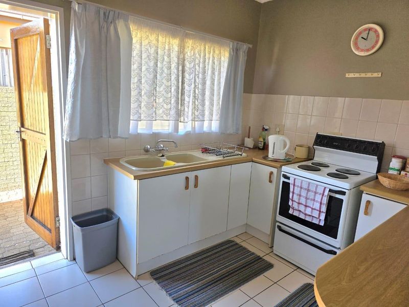 A functional kitchen featuring a double basin sink, tiled splashback, laminate countertops, and a freestanding electric stove with direct access to an outdoor area.