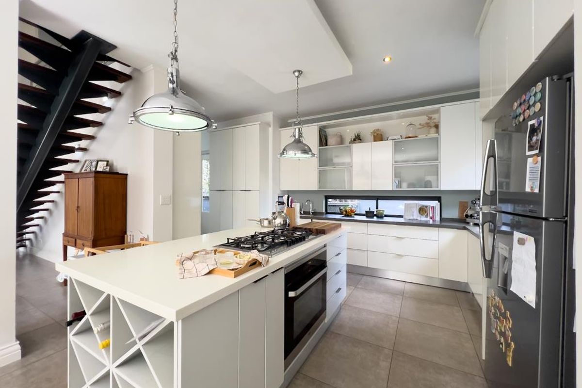 Modern kitchen featuring a central island with a built-in gas hob and oven, sleek white cabinetry, and large format floor tiles.