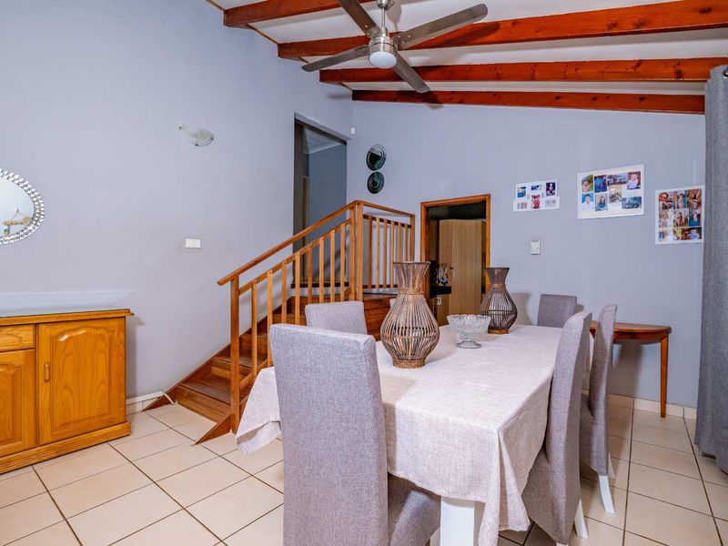Dining area featuring exposed timber ceiling beams, a ceiling fan, tiled flooring, and a wooden staircase leading to the upper level.