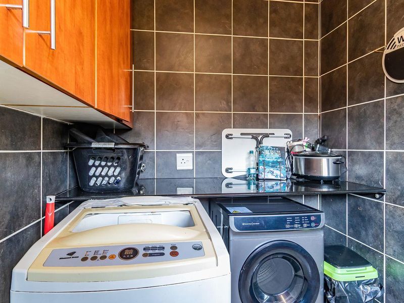 A functional laundry area featuring dark tiled walls, granite countertops, and built-in cabinetry providing practical storage and workspace for laundry appliances.
