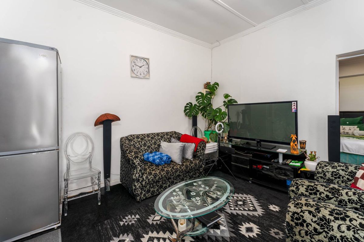 A compact living room area featuring neutral walls and direct access to an adjacent bedroom.