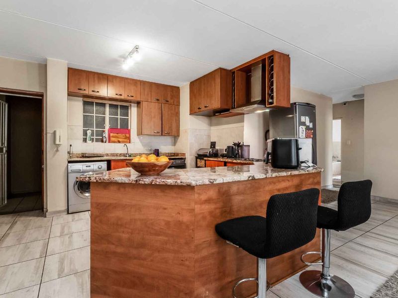 A functional kitchen featuring wooden cabinetry, granite countertops, and tiled flooring, with an open-plan layout connecting to the living area.