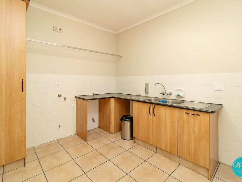 A functional laundry room featuring built-in cabinetry, a stainless steel sink, tiled splashbacks, and dedicated plumbing connections for appliances.