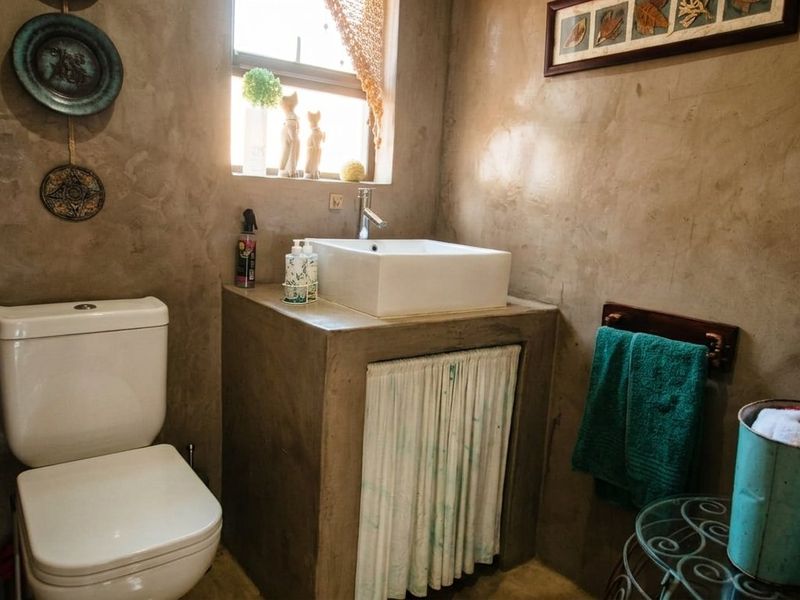 A compact bathroom featuring a custom cement vanity with a vessel sink, chrome faucet, and a modern toilet against textured cement walls.