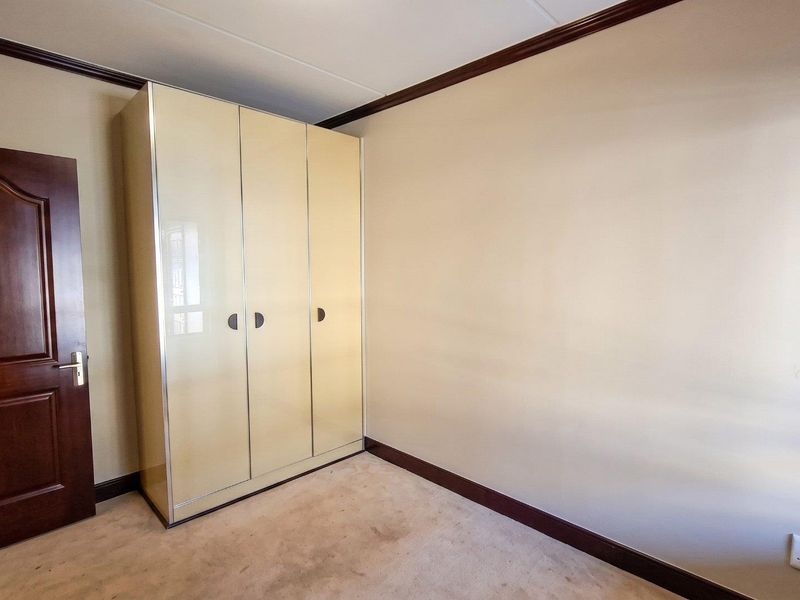 A vacant bedroom featuring a built-in wardrobe, dark wood-toned door and trim, and neutral wall finishes.