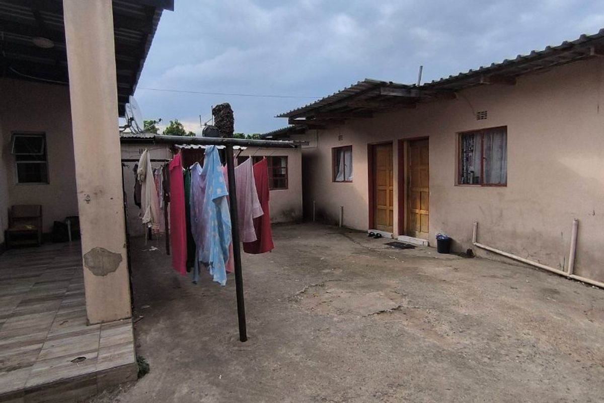 Rear courtyard area featuring a concrete patio, tiled veranda, and access to multiple exterior doors under a corrugated metal roof structure.