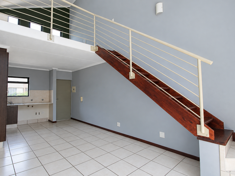 Open plan living area featuring a mezzanine level, tiled flooring, and a functional kitchen space with built-in cabinetry and a wooden staircase.