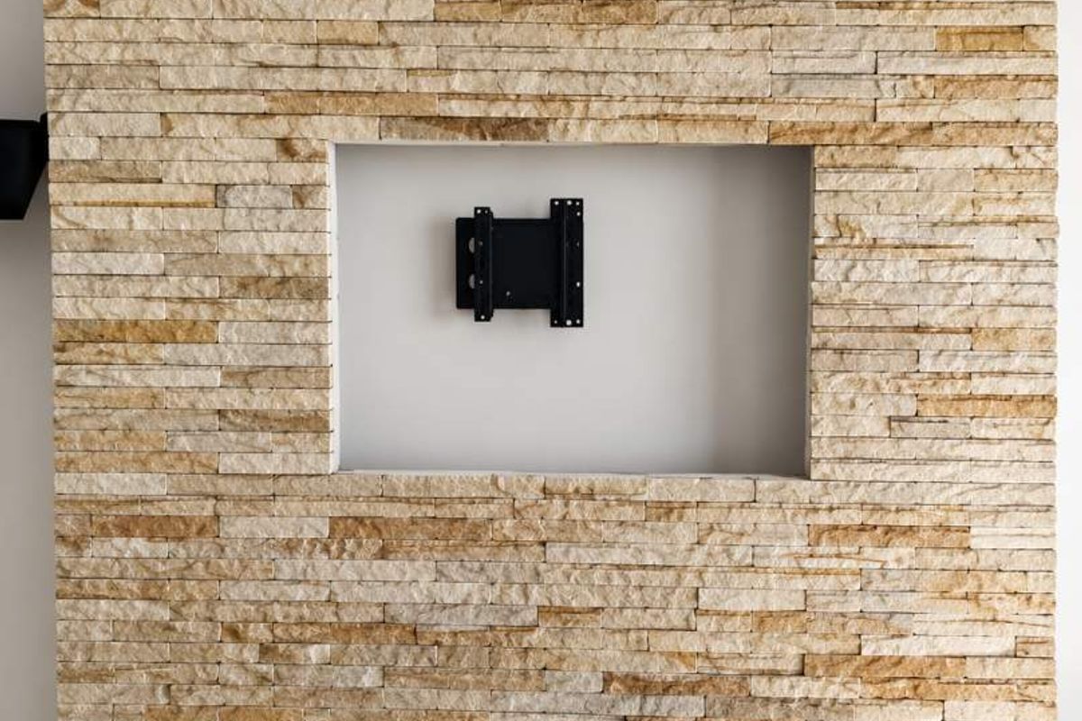 A modern living room feature wall finished in natural stacked stone with a dedicated recessed niche and integrated television mounting bracket.