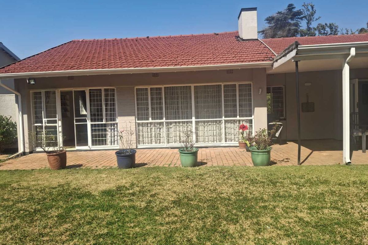 Rear view of the house featuring a paved patio area, sliding glass doors with security gates, and a tiled roof with a brick chimney.