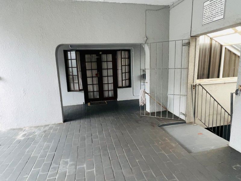 Covered entrance area featuring paved flooring, a security gate, and timber-framed glass doors leading into the apartment.