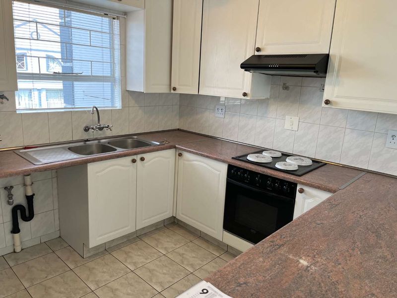 A functional kitchen featuring white cabinetry, laminate countertops, a double basin sink, and built-in cooking appliances with tiled flooring and backsplash.