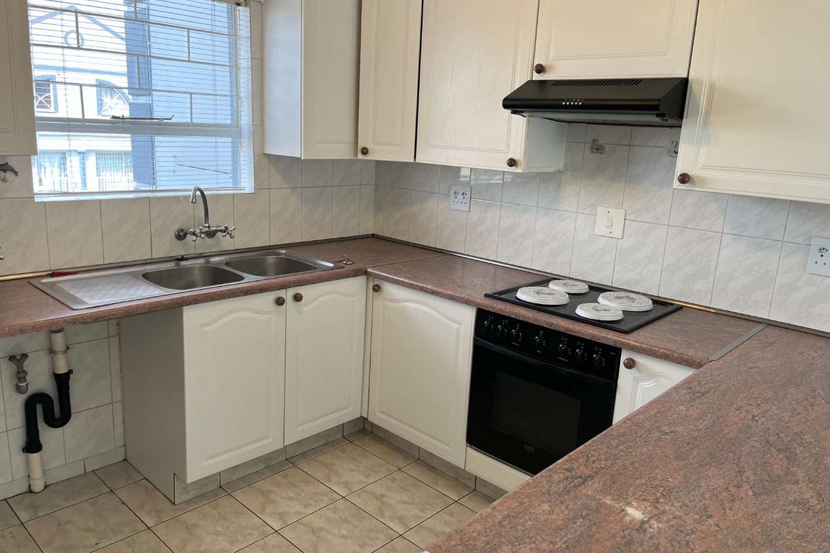 A functional kitchen featuring white cabinetry, laminate countertops, a double basin sink, and built-in cooking appliances with tiled flooring and backsplash.