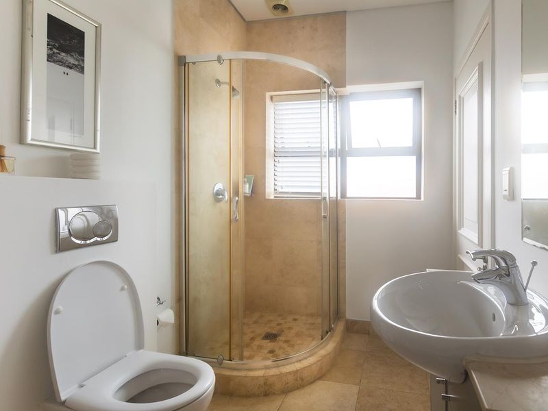 A well-maintained bathroom featuring a curved glass shower enclosure, wall-mounted toilet, and a modern pedestal basin with chrome fixtures.
