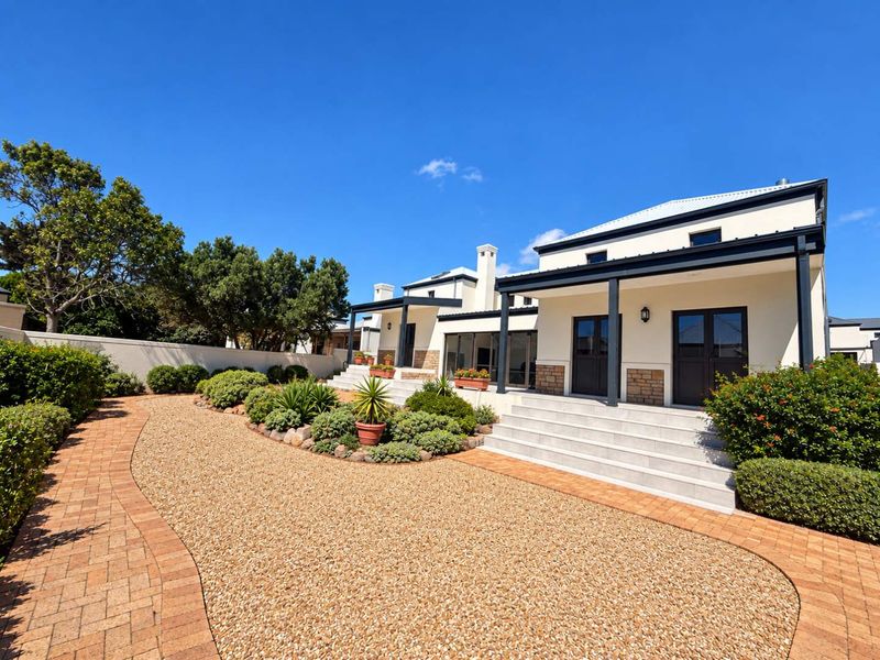 A well-maintained rear exterior view featuring a covered patio, stone-clad accents, paved walkways, and landscaped garden beds.