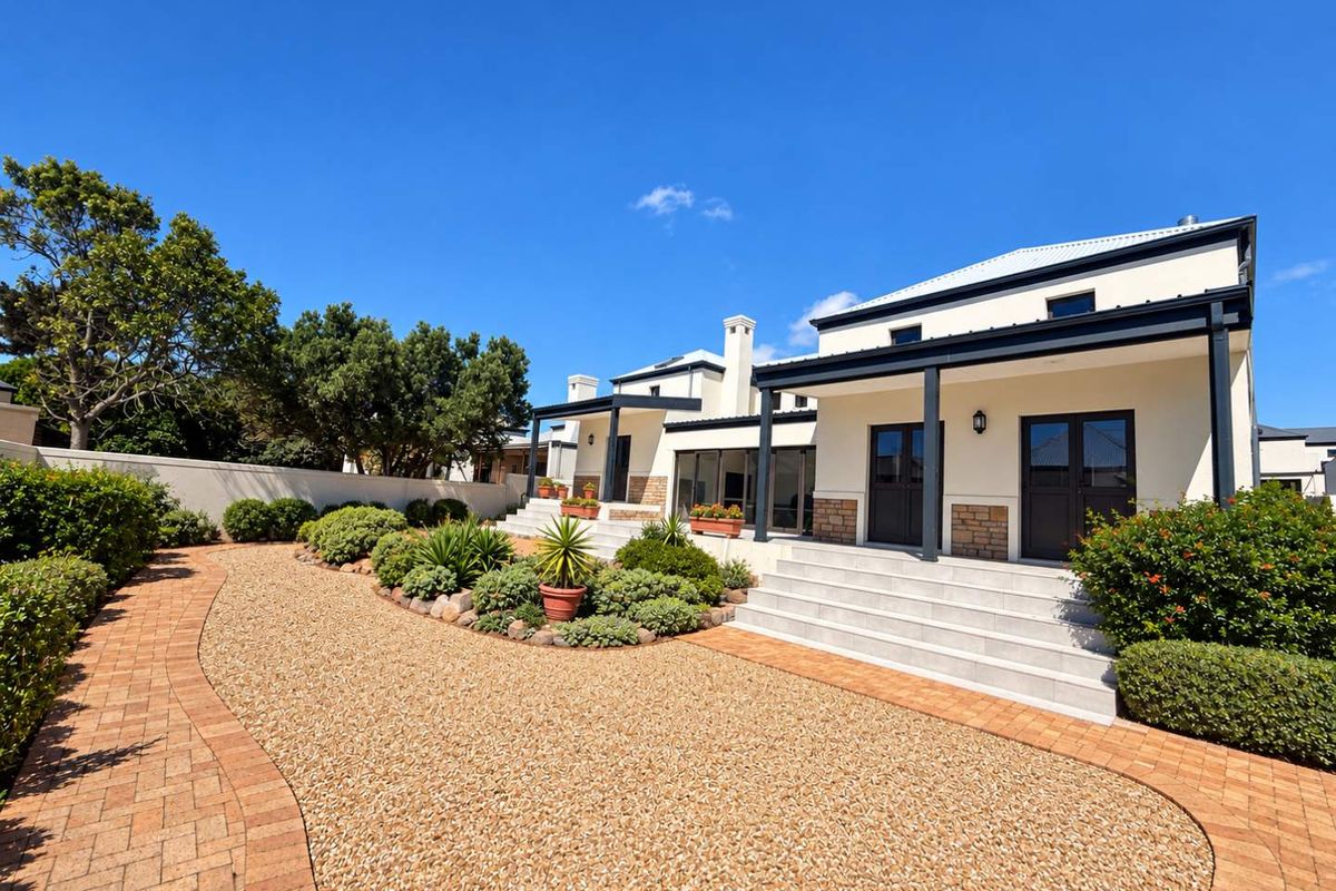 A well-maintained rear exterior view featuring a covered patio, stone-clad accents, paved walkways, and landscaped garden beds.