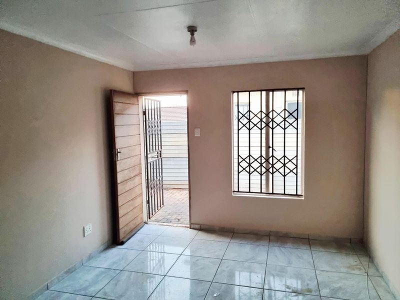 An empty living room featuring tiled flooring, security bars on the window, and a security gate leading to the exterior.
