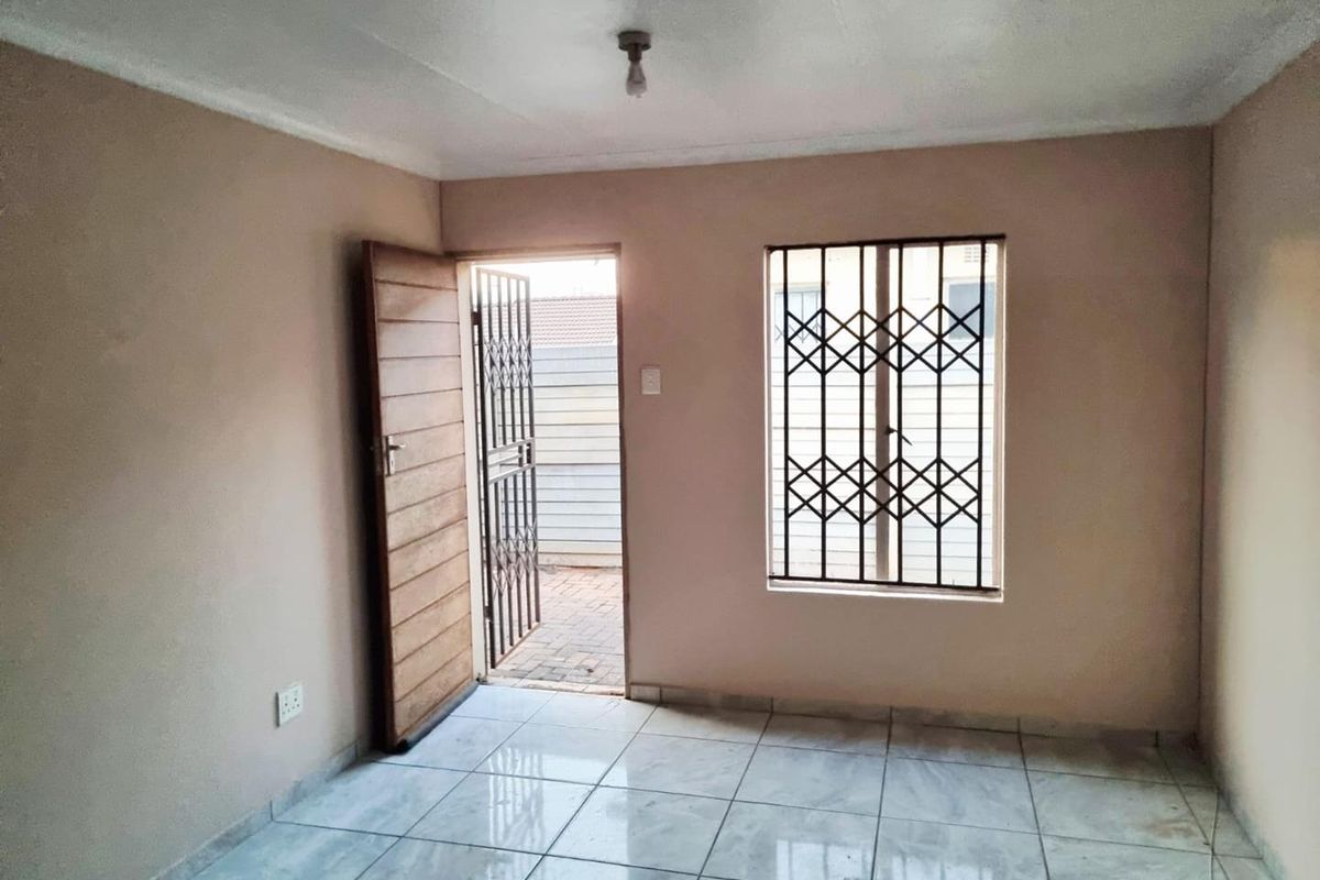 An empty living room featuring tiled flooring, security bars on the window, and a security gate leading to the exterior.
