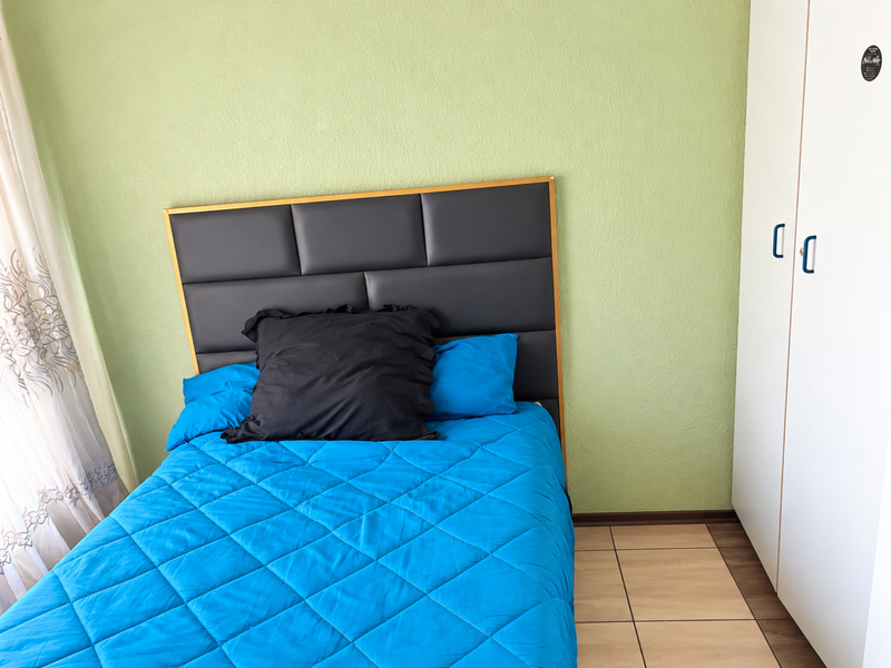 A bedroom featuring light green walls, tiled flooring, and a built-in white wardrobe.