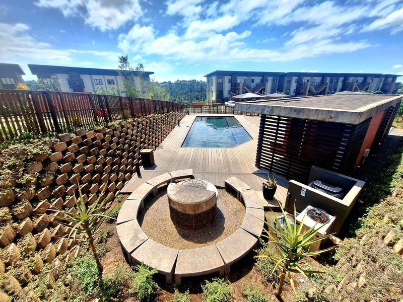 Outdoor pool area featuring a swimming pool, timber decking, and a circular built-in fire pit with surrounding seating.