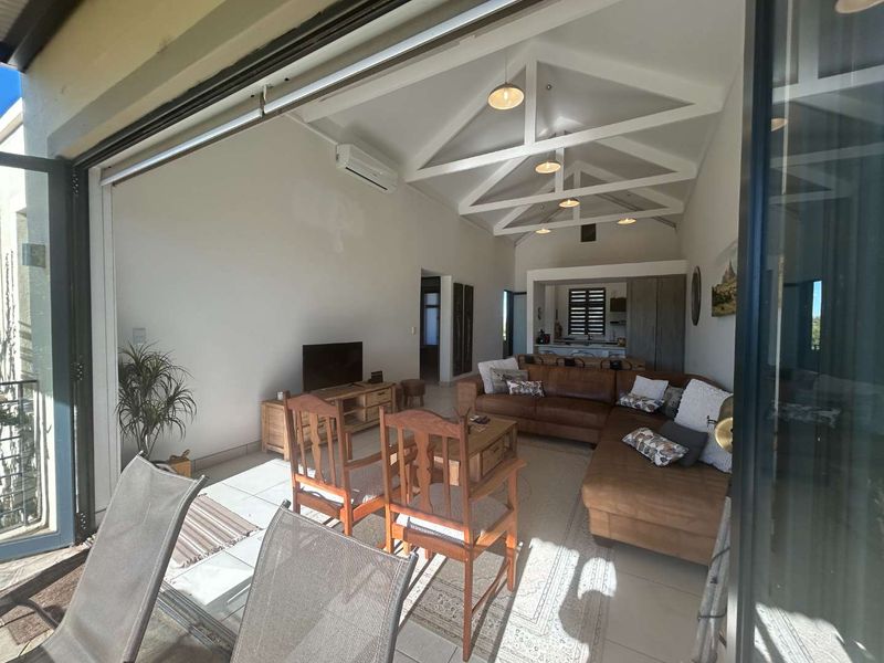 Spacious open-plan living area featuring a high vaulted ceiling with exposed trusses, tiled floors, and large stacking doors opening to an outdoor space.