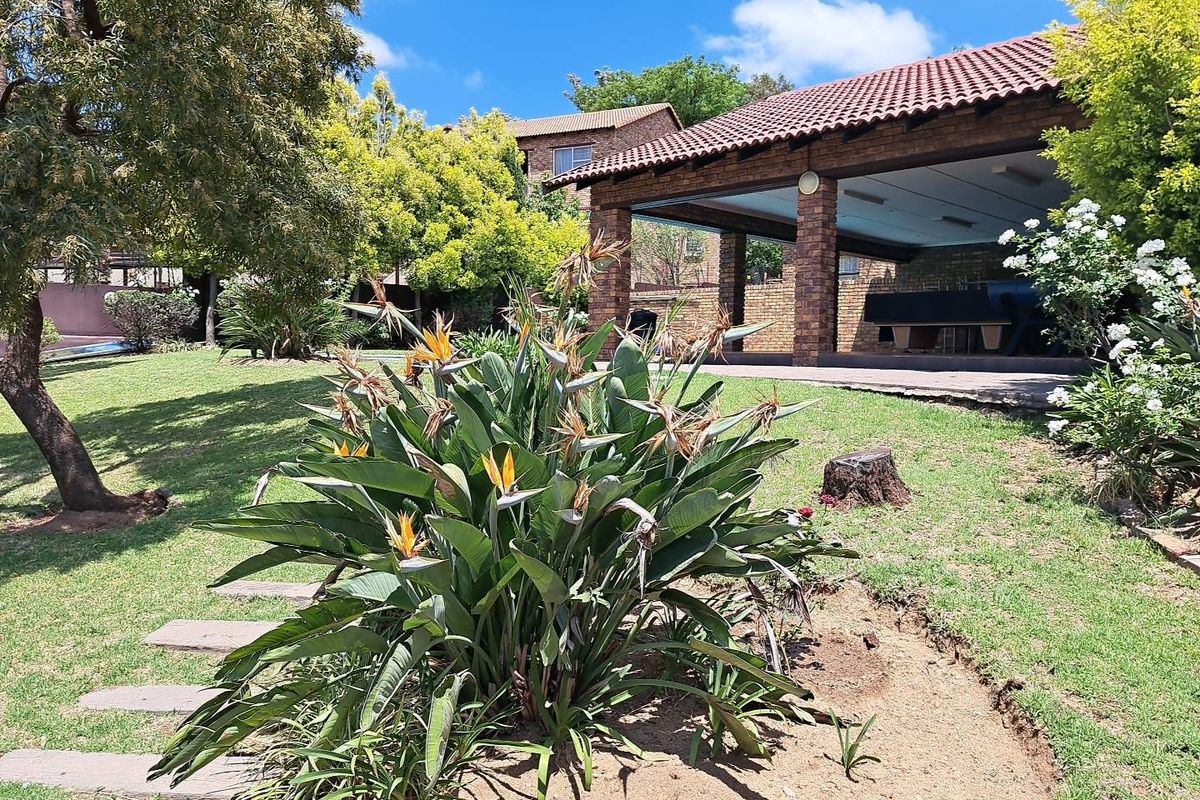 A spacious rear garden featuring a large covered patio with brick pillars, mature trees, and a well-maintained lawn area.