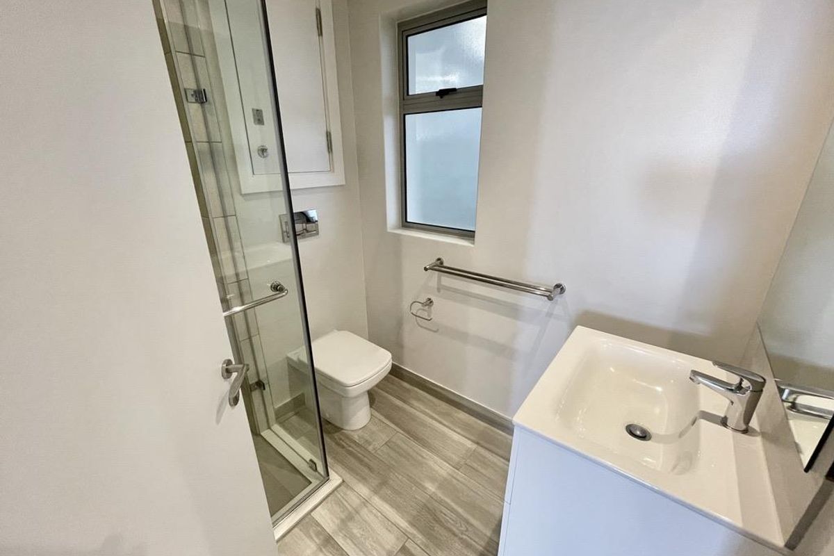 A modern bathroom featuring a glass-enclosed shower, a white vanity with a basin, a toilet, and wood-look tiled flooring.