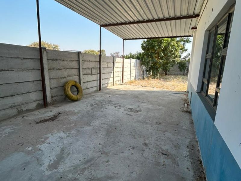 A covered outdoor patio area featuring a corrugated metal roof, concrete flooring, and a precast concrete boundary wall.