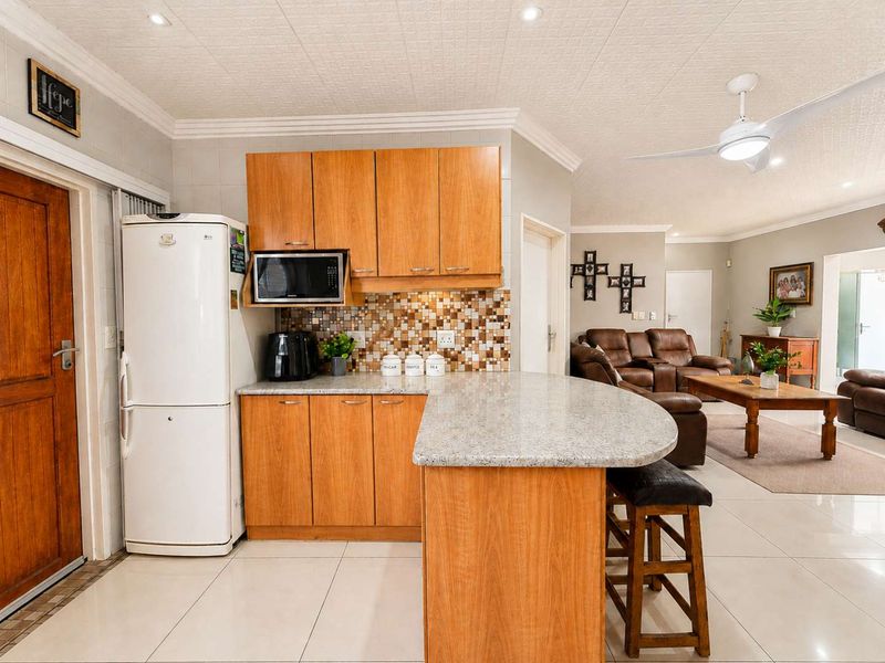 Open-plan kitchen featuring wooden cabinetry, granite countertops, and a mosaic tile backsplash, seamlessly flowing into the adjacent living area.