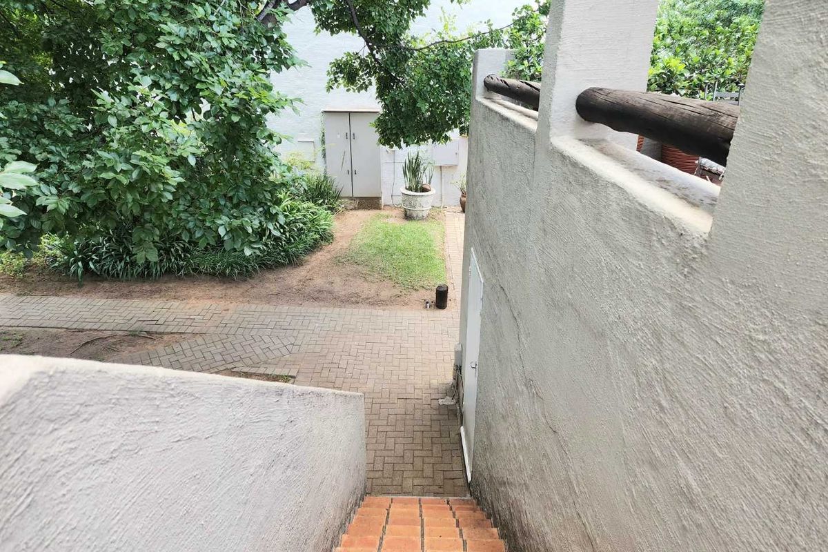 A view looking down a staircase towards a paved rear garden area with mature trees and a small storage structure.