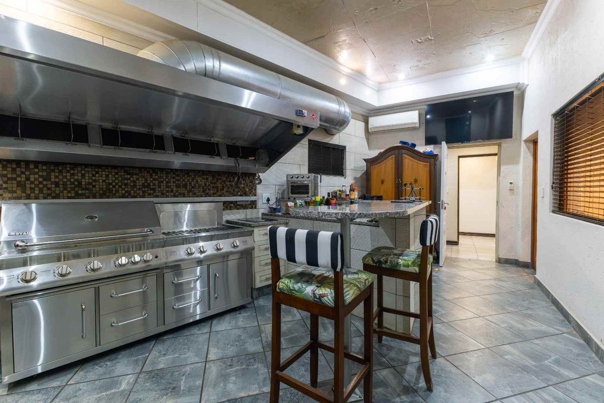 Spacious kitchen featuring a large commercial-style stainless steel range, industrial extractor hood, granite breakfast bar, and durable tiled flooring.