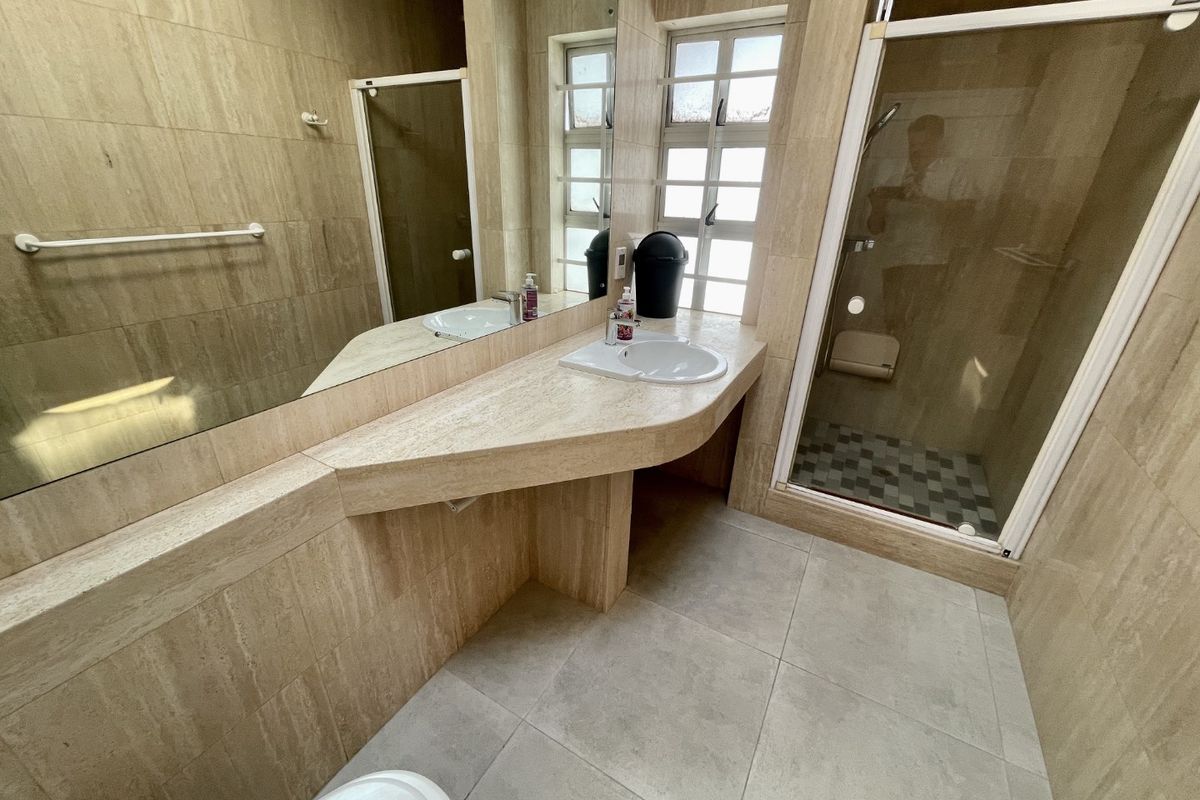 A functional bathroom featuring floor-to-ceiling travertine tiling, a built-in vanity with integrated basin, a large wall mirror, and a separate glass-enclosed shower.