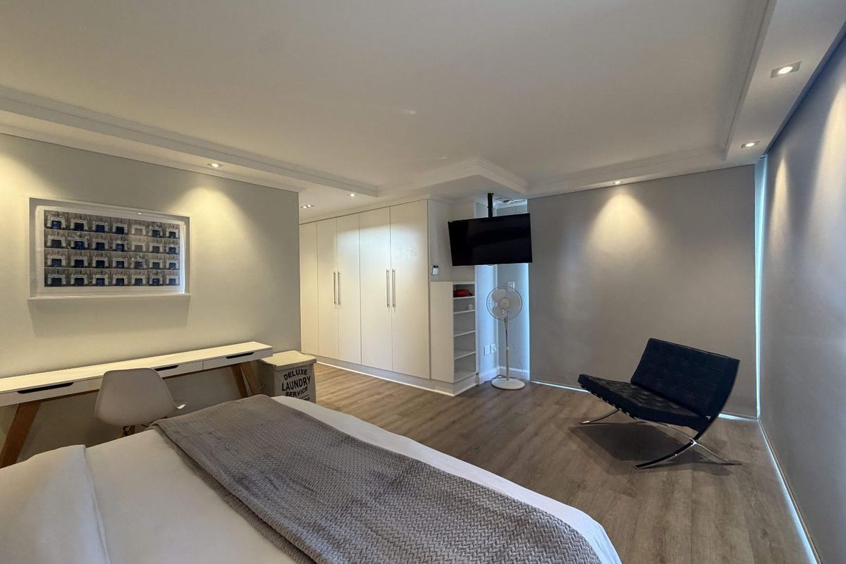 Modern bedroom featuring laminate flooring, built-in cupboards, recessed downlighting, and neutral wall finishes.
