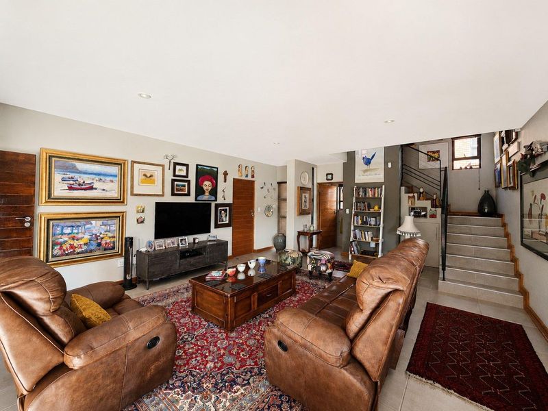Spacious open-plan living area featuring tiled floors, recessed lighting, and a staircase with a modern metal railing leading to the upper level.