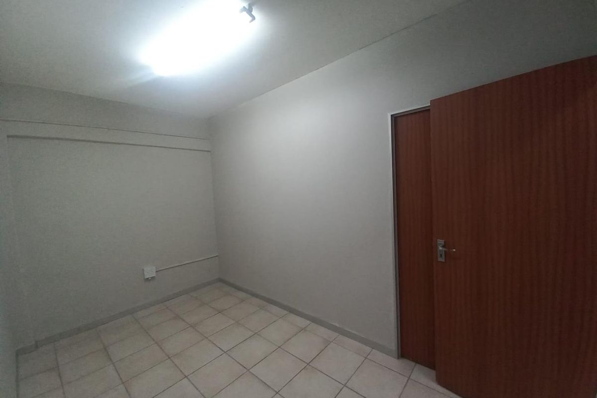 A vacant bedroom featuring neutral wall finishes, tiled flooring, and a standard timber door, providing a blank canvas for office or residential use.