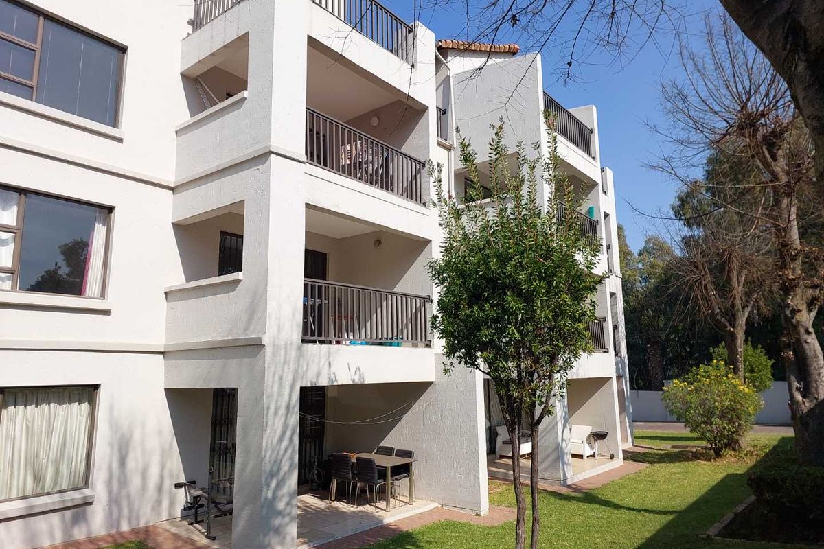 Rear elevation of a multi-story apartment building featuring stacked balconies, ground-floor patios, and a well-maintained communal garden area.